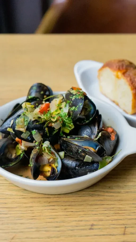 Close-up of steamed mussels with open shells, garnished with green herbs.