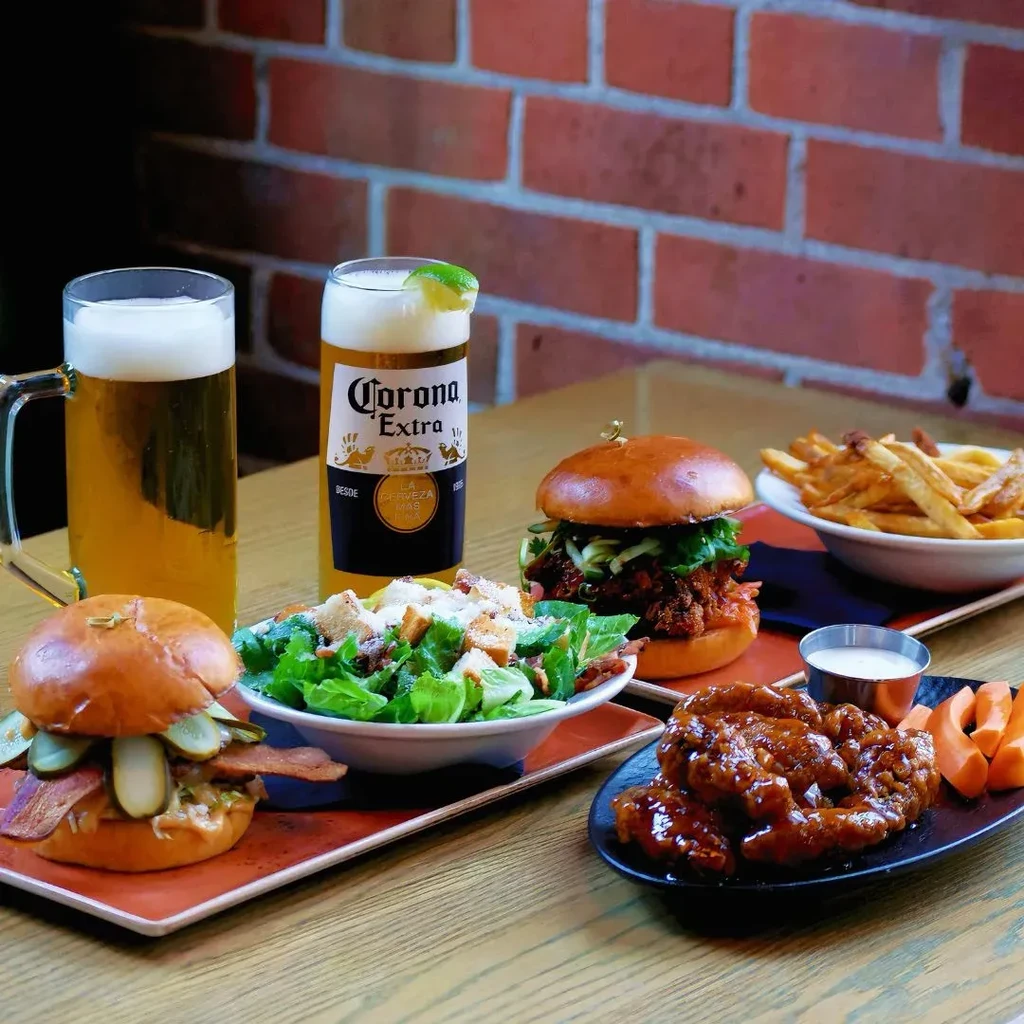 A table full of burgers, salad, fries, chicken wings, and beer.