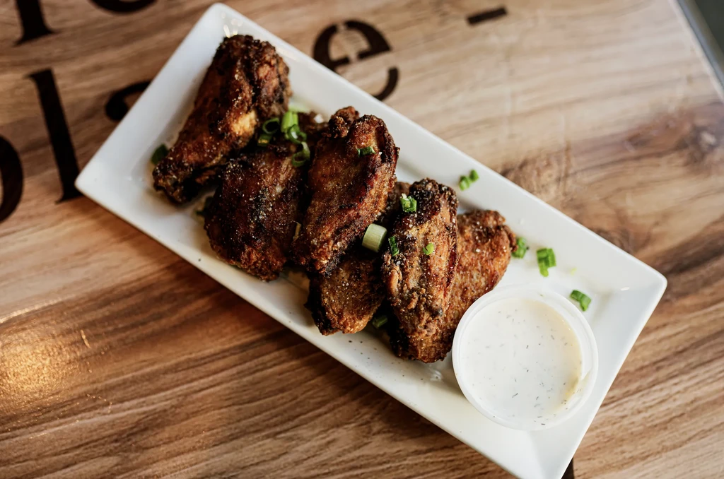 Crispy fried chicken wings with scallions and dipping sauce on wood.