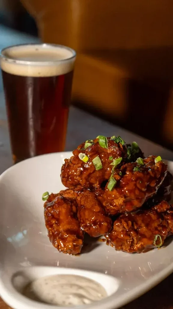 Close-up of sau saucy chicken wings, dipping sauce, and a foamy beer.