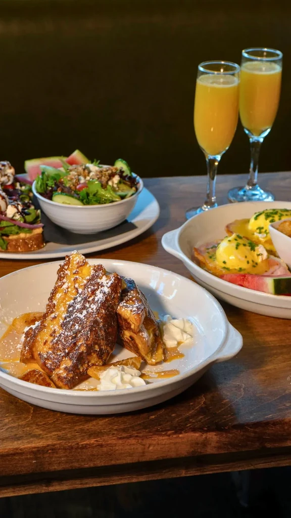 Vibrant brunch spread with French toast, Eggs Benedict, salad, and mimosas.
