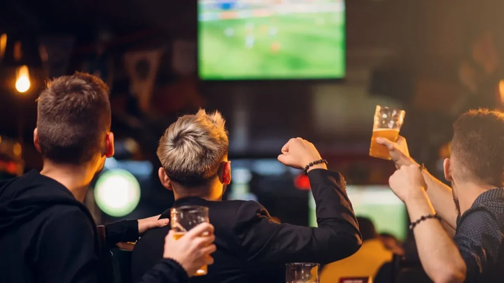 Enthusiastic men from behind watch a soccer game in a bar.