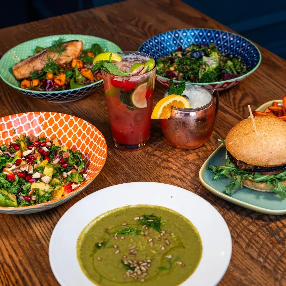 Rustic table with grilled salmon, salads, soup, burger, fries, and drinks.