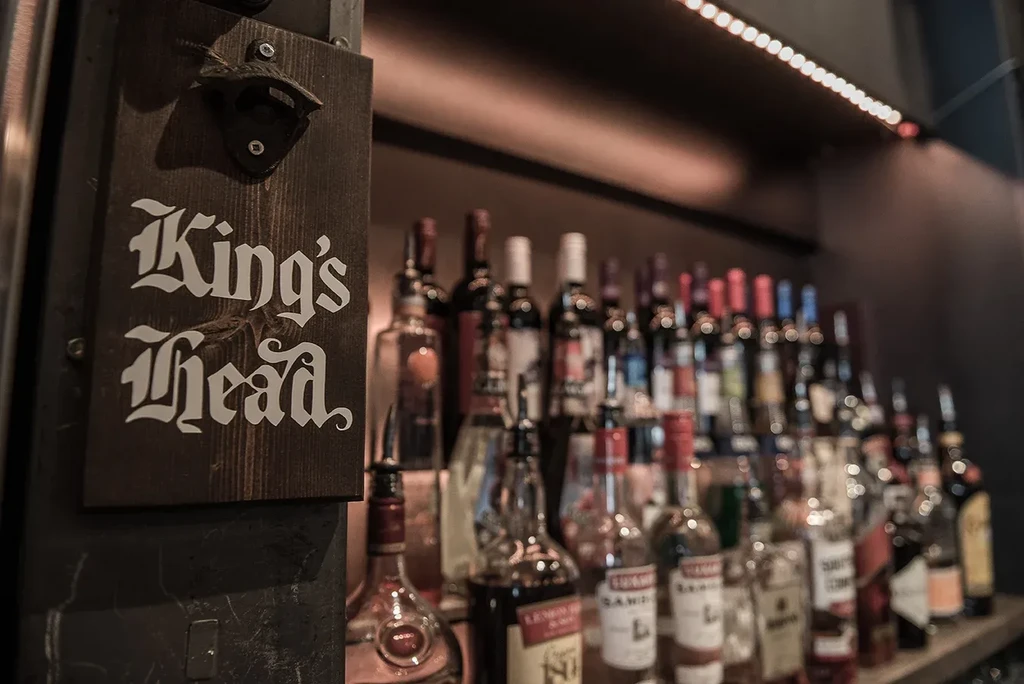 King's Head sign with bottle opener and blurred bar bottles.