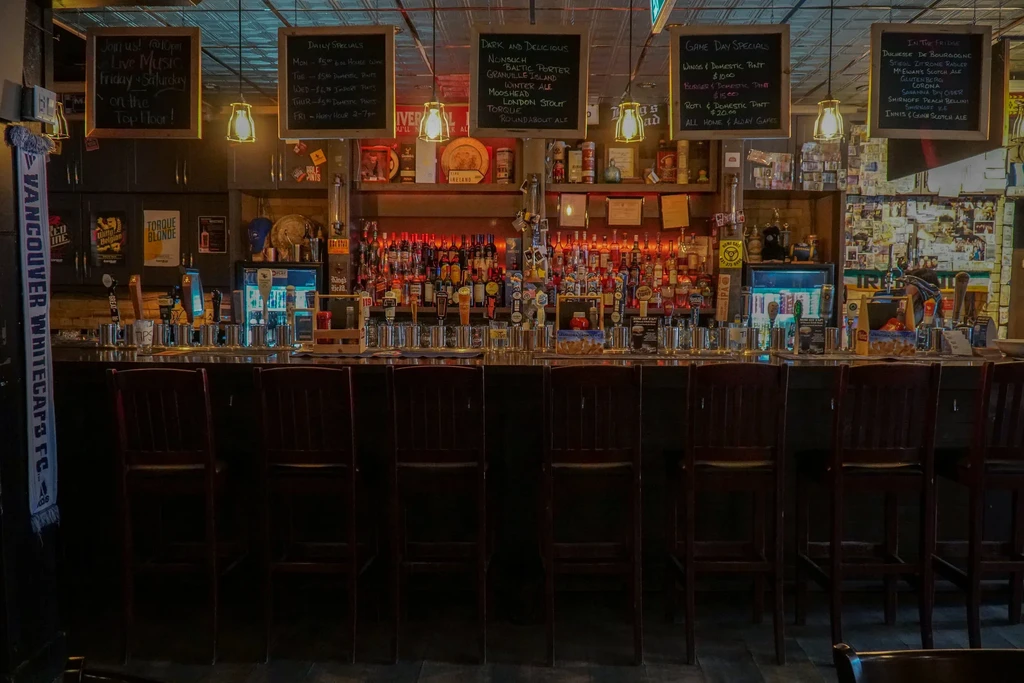 Dimly lit bar with numerous beer taps, liquor bottles, and chalkboards.