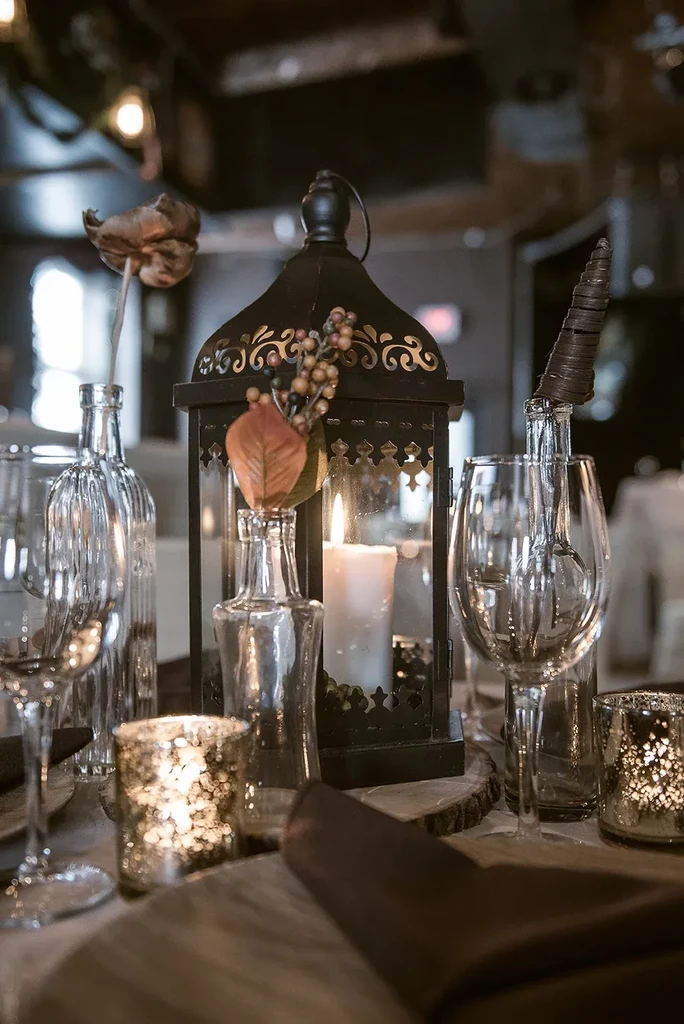 Rustic table setting featuring a lit lantern, candles, and glass bottles.