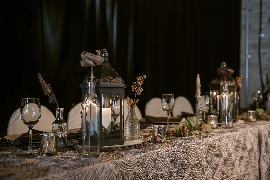 Beautifully set table with ornate lanterns, candles, glass, and dried flowers.