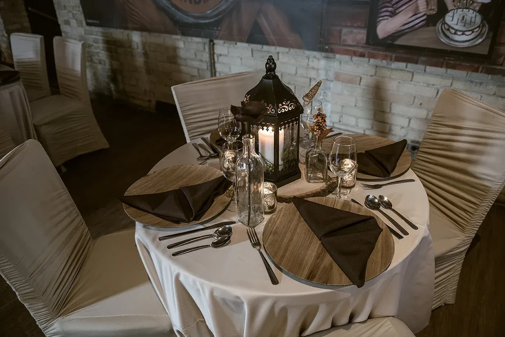 Round dining table with wooden chargers, black lantern centerpiece, and ambient lighting.