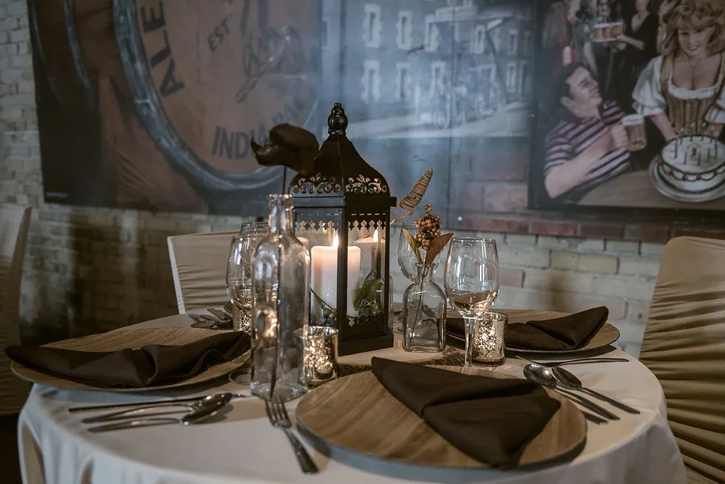 Set dining table with lit lantern centerpiece and pub-themed brick wall.