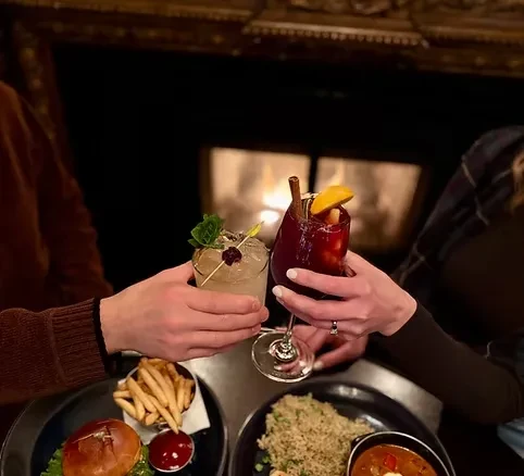 Two people toast cocktails and dinner in a cozy restaurant.
