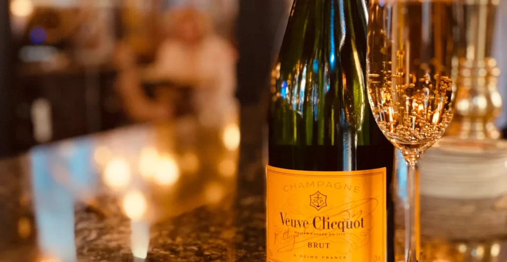 Veuve Clicquot champagne bottle and flute on a dark reflective surface.