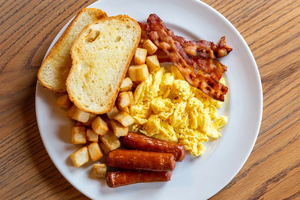 Hearty breakfast plate: scrambled eggs, bacon, sausage, home fries, buttered toast.