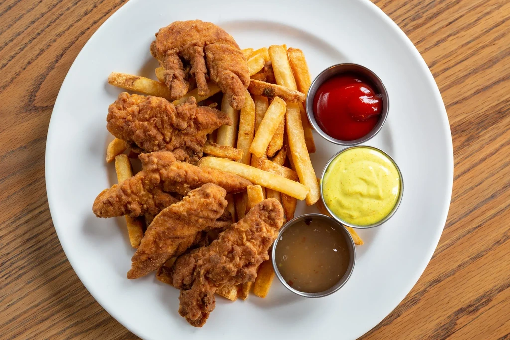 Crispy chicken tenders, fries, ketchup, mustard, and brown sauce on a plate.
