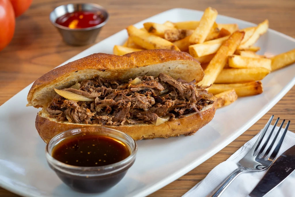 Beef sandwich with fries, au jus, and ketchup on a plate.