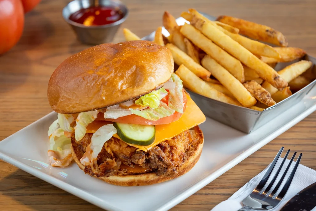 Golden fried chicken sandwich, fries, and sauce on a wooden table.