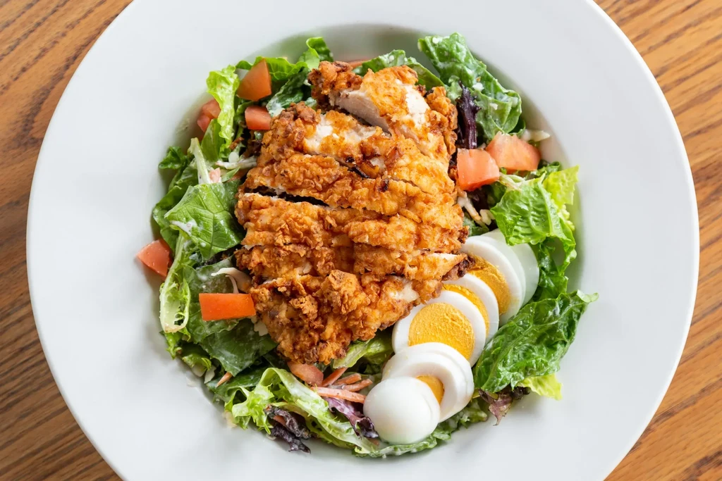 Sliced fried chicken salad with lettuce, tomatoes, and hard-boiled egg.