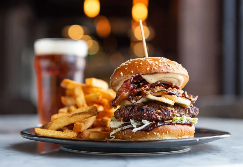 Gourmet double-patty burger, golden fries, and amber beer on a dark plate.