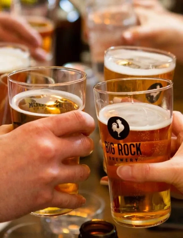 Hands holding beer glasses in a toast, Big Rock Brewery logo visible.