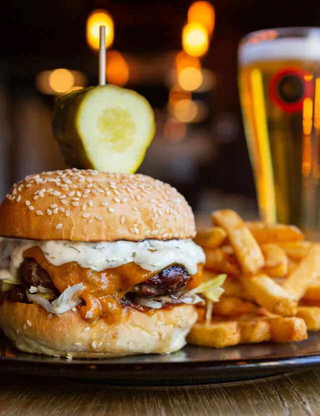 A gourmet hamburger, fries, and beer in a restaurant setting.