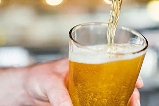 Hand holds glass as golden beer is poured, creating foam.
