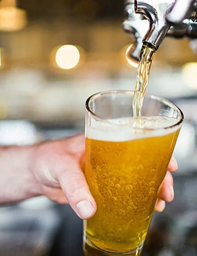 Hand holds glass filling with golden beer from a chrome tap.