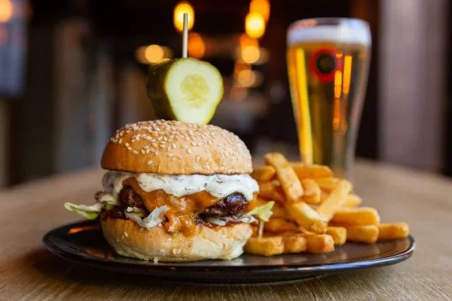 Close-up of a gourmet burger, fries, and beer in a restaurant setting.