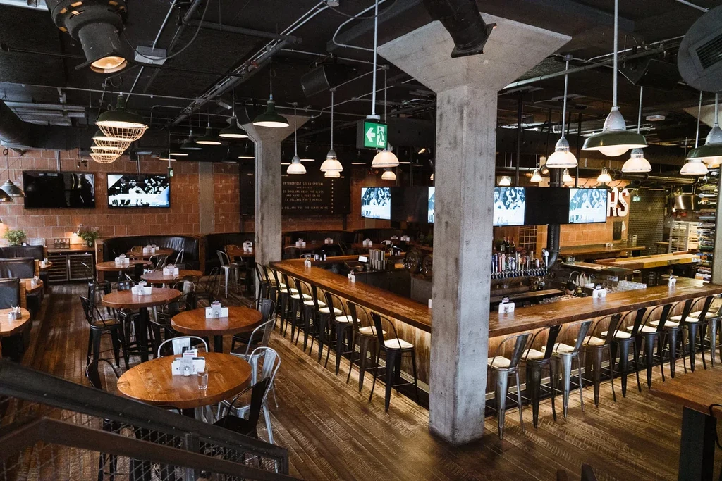 Empty industrial-chic bar and restaurant interior with tables and TVs.