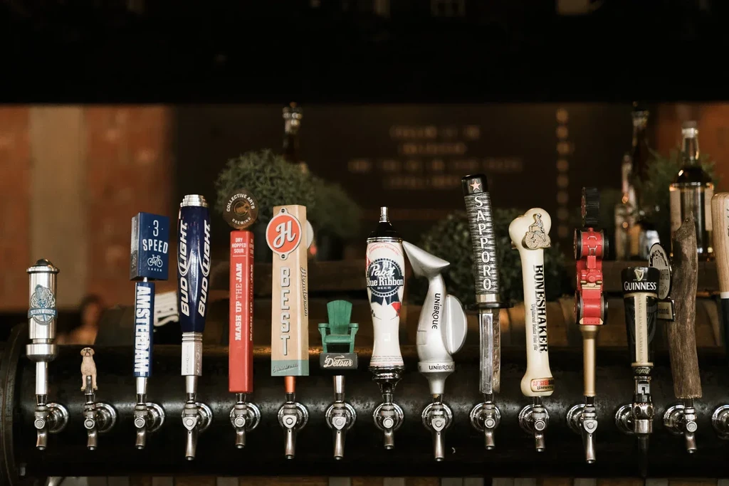 Diverse branded beer tap handles in a row at a bar.