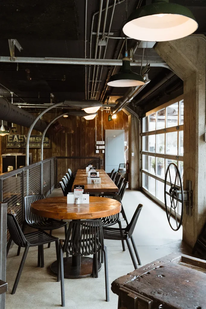 Industrial-rustic restaurant interior with exposed ceiling, green lights, wooden tables.
