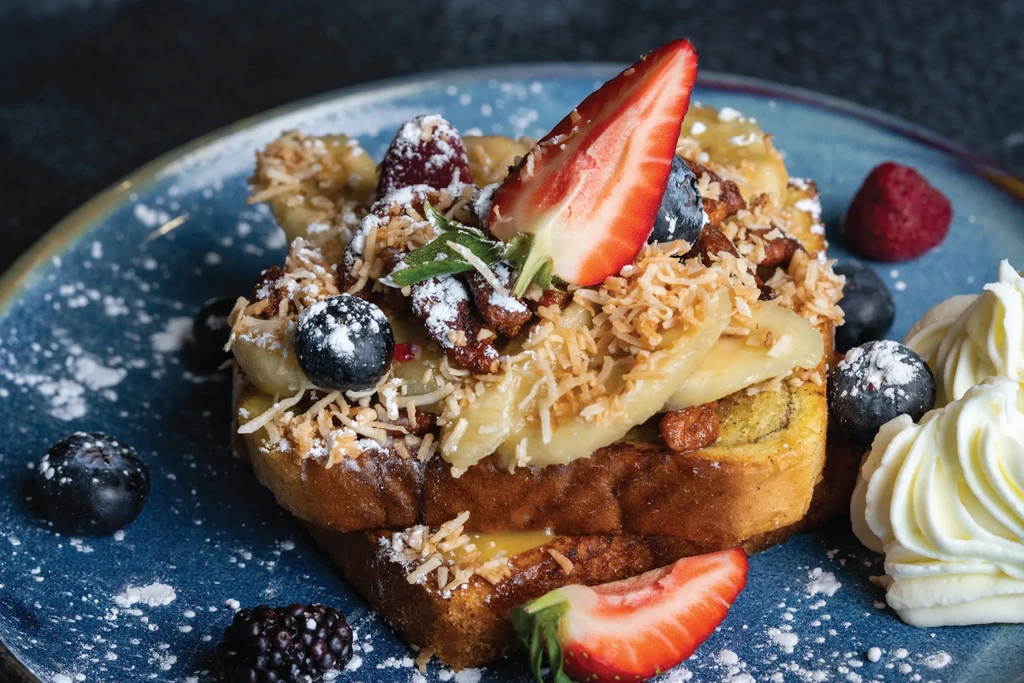 French toast with bananas, berries, coconut, nuts, whipped cream, powdered sugar.