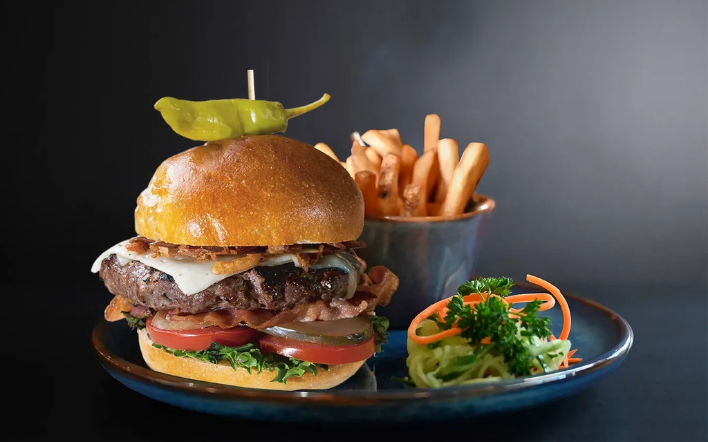 Gourmet burger, golden fries, and side salad on a dark plate.
