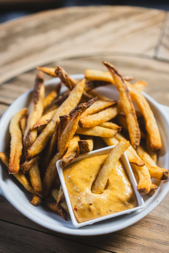 Overflowing bowl of rustic fries with a fry dipped in creamy sauce.