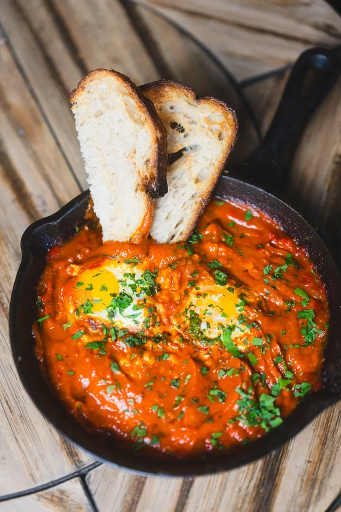 Cast-iron skillet of red sauce with poached eggs, herbs, and bread.