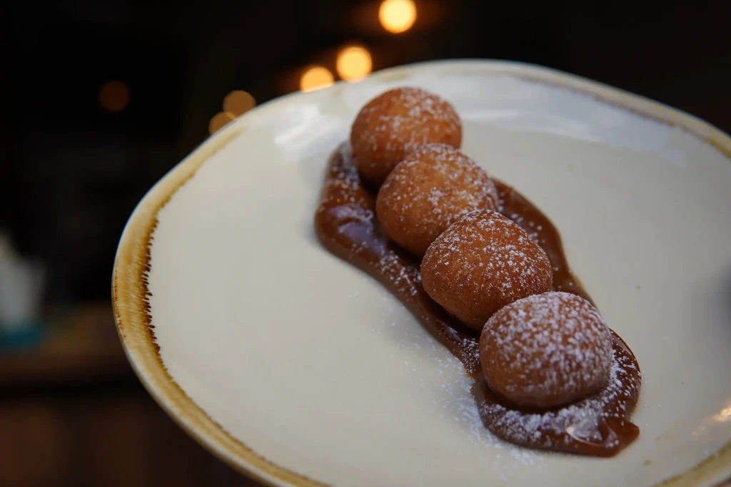 Four golden-brown fried dough balls with powdered sugar on caramel sauce.