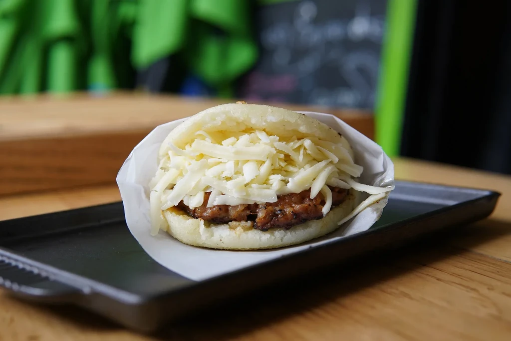 Arepa with shredded meat and cheese, partially wrapped in paper.