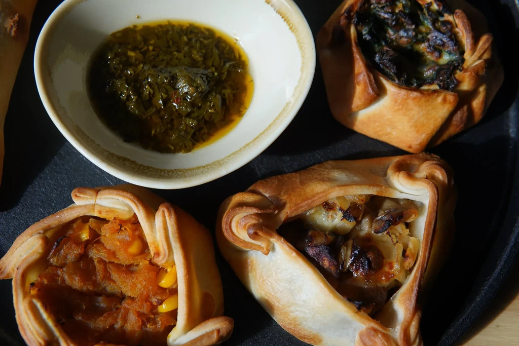 Three baked pastries with green, orange, and golden fillings; green dipping sauce.