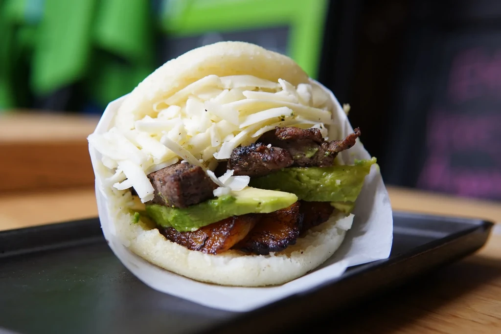 Close-up of arepa filled with white cheese, grilled meat, avocado, plantains.