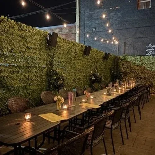 Empty outdoor dining area at night, ivy wall, string lights, and candles.