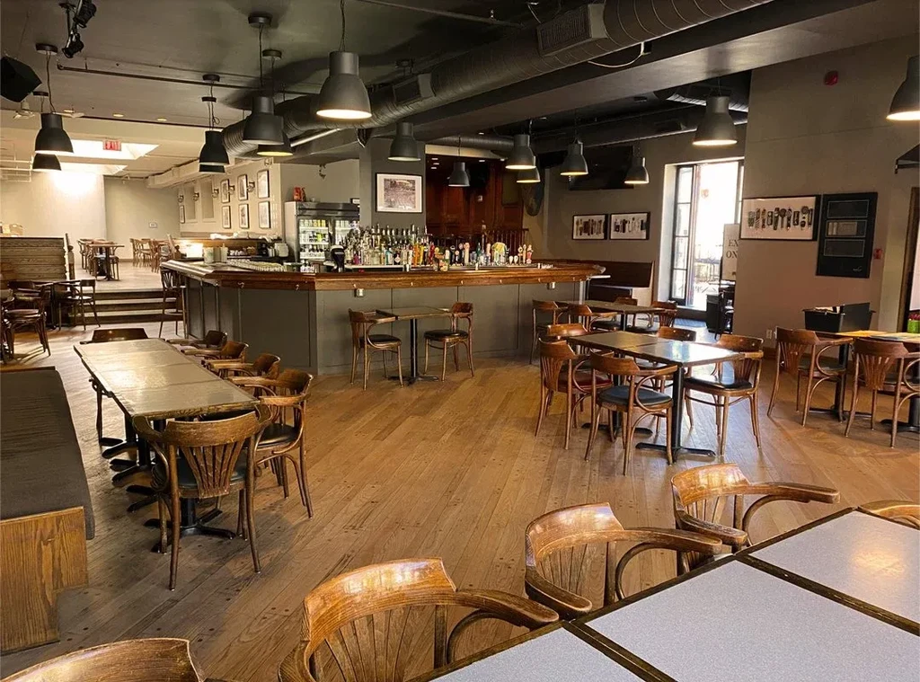 Empty, rustic-industrial restaurant interior with a prominent bar and diverse seating.
