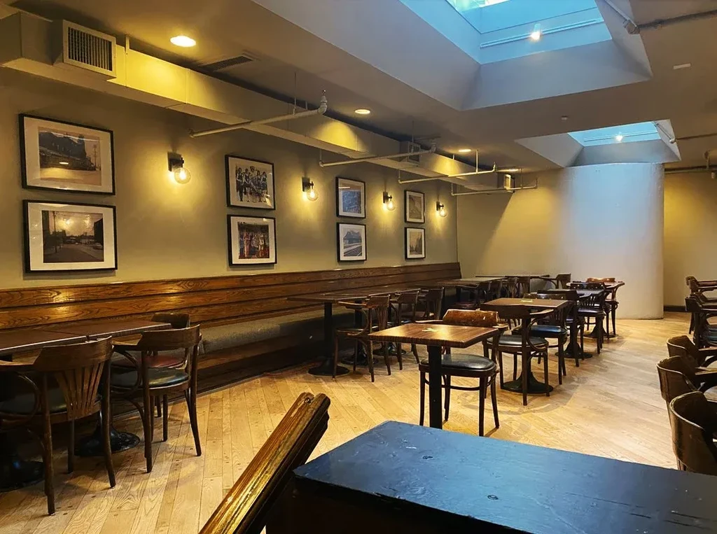 Empty dining room with wooden tables, chairs, bench, photos, and skylight.