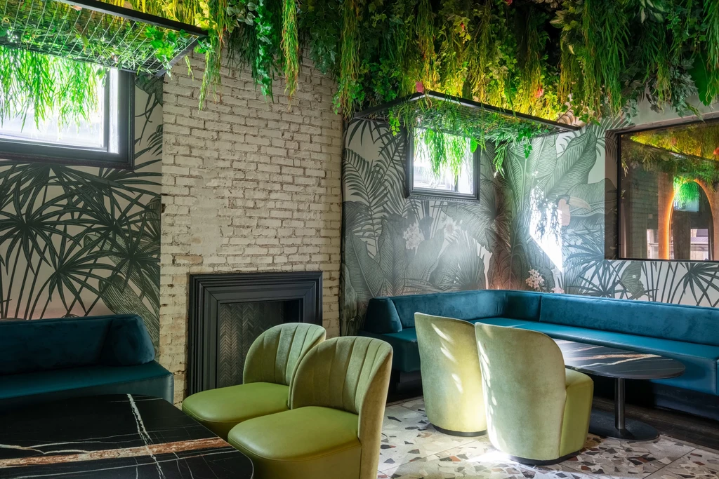 Lush restaurant interior with hanging foliage, velvet seating, and tropical wallpaper.