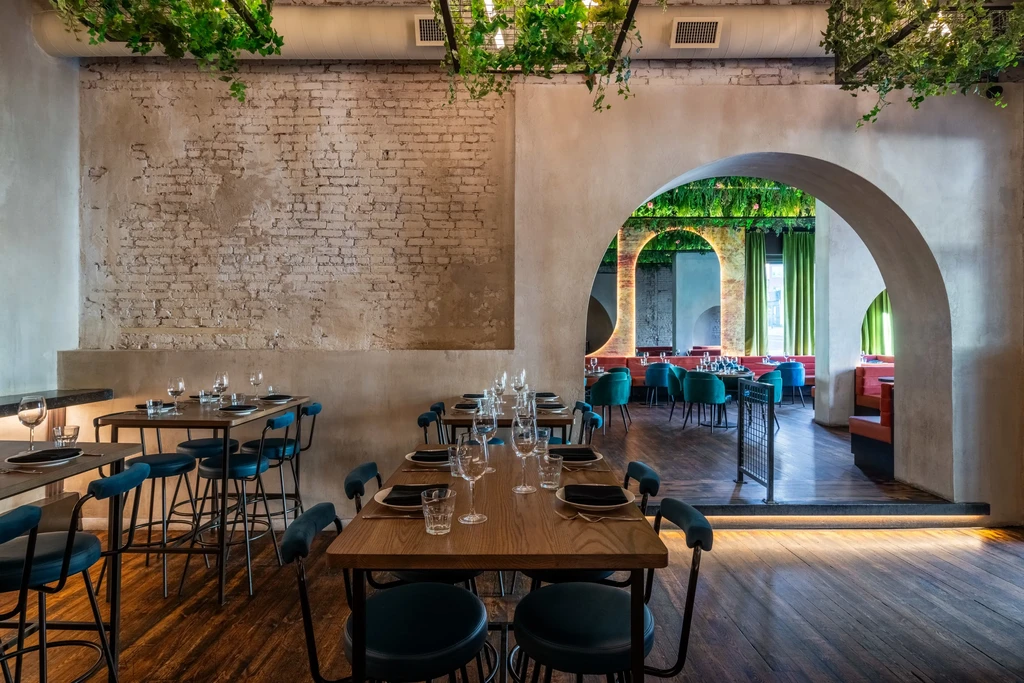 Modern restaurant with illuminated arched dining areas and overhead foliage.
