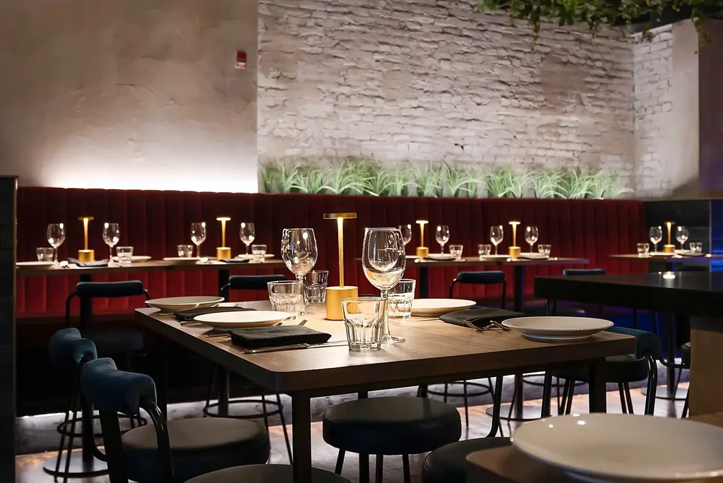 Modern restaurant interior with set tables, red velvet bench, golden lamps.
