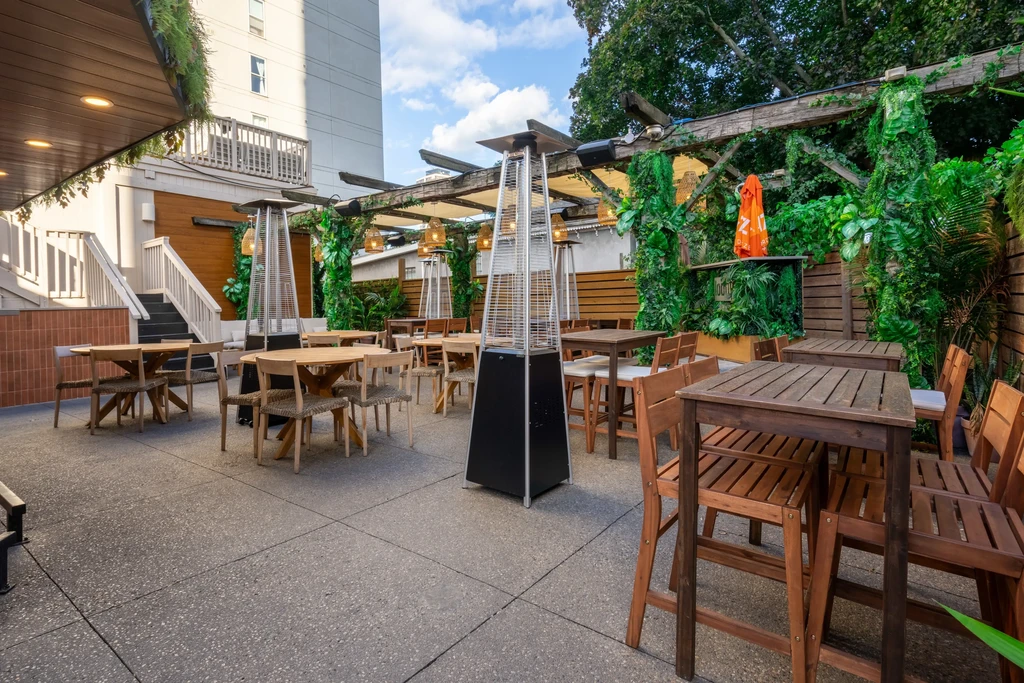 Empty outdoor patio with wooden tables, chairs, plants, and heaters.