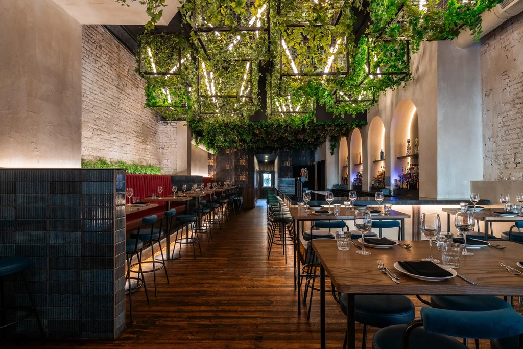 Modern restaurant interior with botanical ceiling, red booths, and long bar.