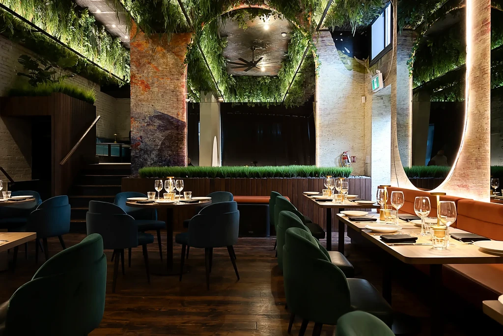 Modern restaurant interior with set tables, dark seating, and hanging greenery.