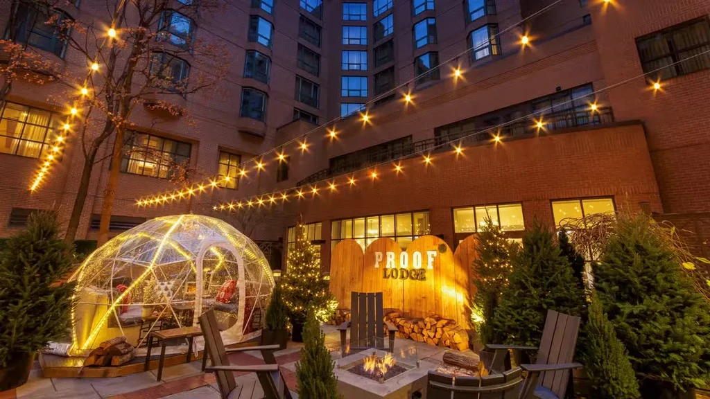 Nighttime lodge patio with lighted dome, fire pit, and 'PROOF LODGE' sign.