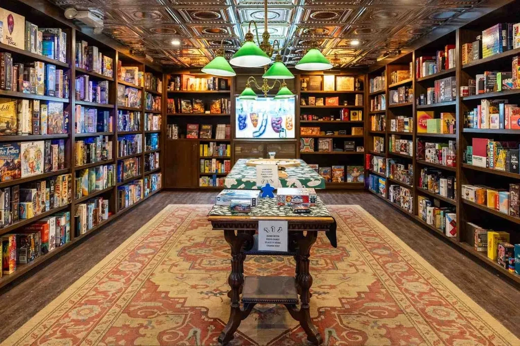 Long room with shelves of board games, two tables, and a chandelier.