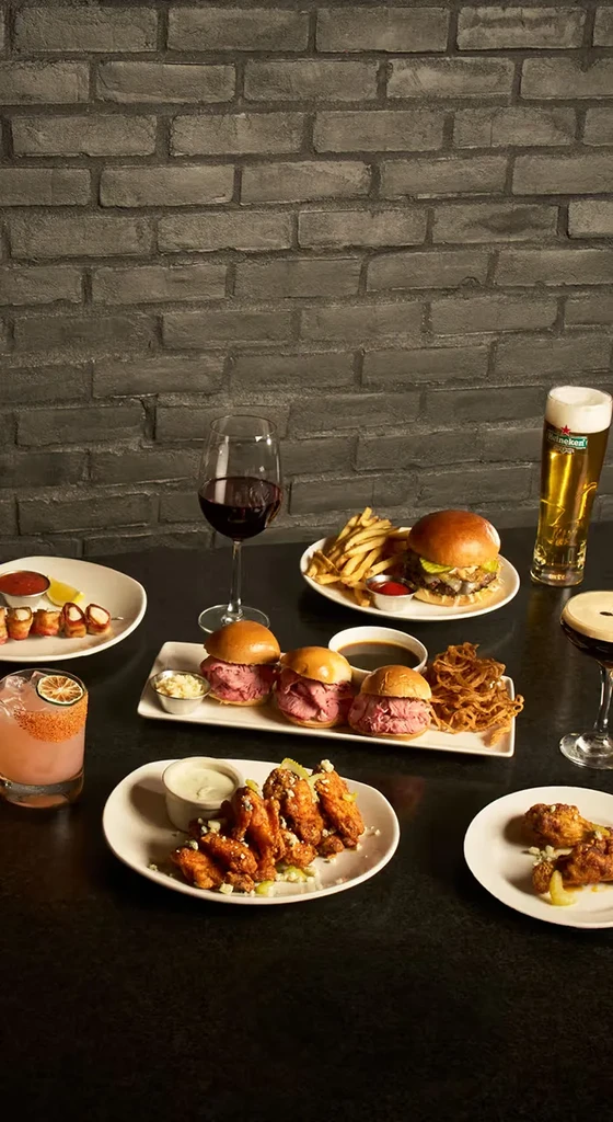 A diverse spread of appetizers, burgers, and drinks on a dark table.
