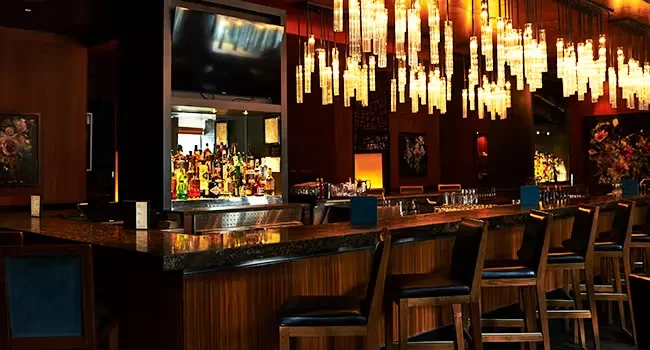 Dimly lit, sophisticated bar with liquor bottles, chandelier, and red walls.